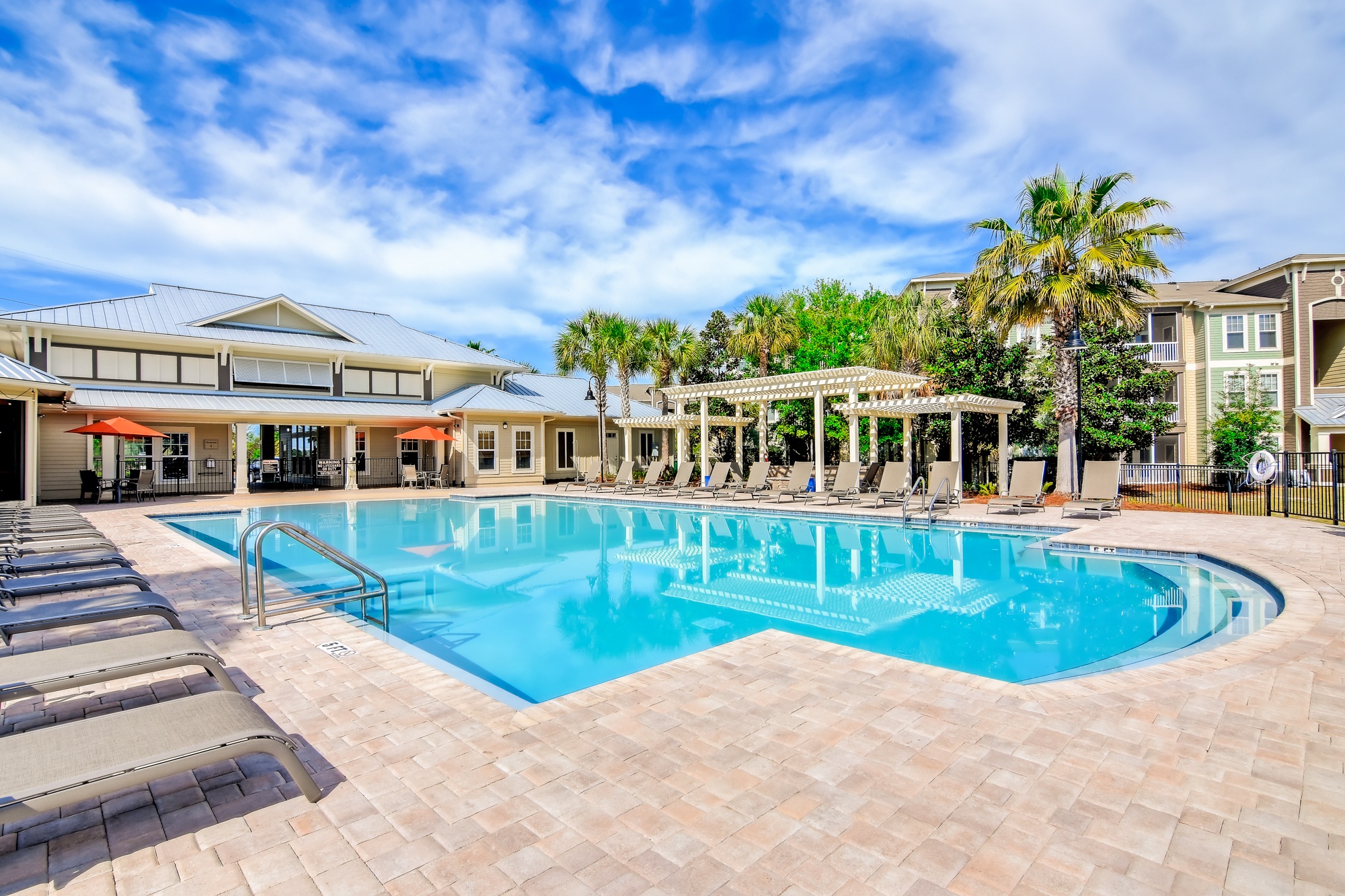 A large outdoor swimming pool surrounded by sun loungers and palm trees.